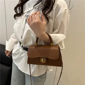 Brown leather crossbody bag with wave flap and gold knob on casual model outfit