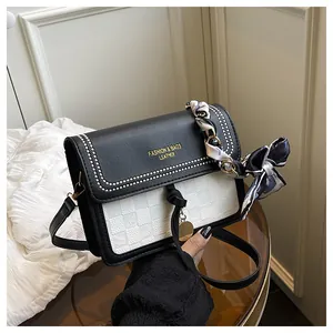 Detail of crossbody bag featuring metal rivets, gold logo and decorative silk scarf handle