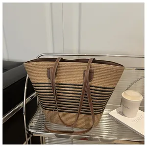 Detail of hand-woven straw tote bag with black stripes and brown leather handles