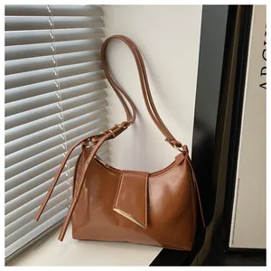 Detail of a brown leather shoulder bag with gold metal trim and unique triangular flap