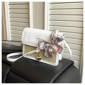 Detail of cream crossbody bag with woven texture, fashion logo and silk scarf charm
