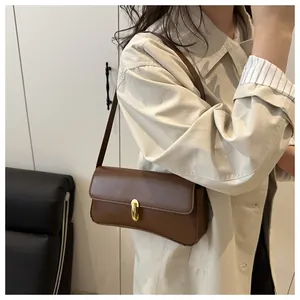 Detail shot of a brown leather shoulder bag with an elegant golden oval buckle closure
