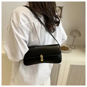 Detail view of a black leather underarm bag with golden clasp worn by a model