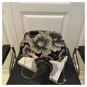 Detailed close-up of intricate gold floral embroidery on a black satin shell bag