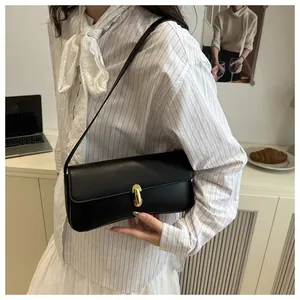 Detail of a black minimalist underarm bag with a golden buckle in a lifestyle setting