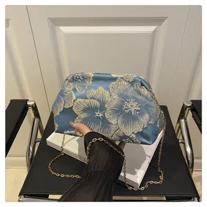 Detail of blue satin cosmetic bag with golden floral embroidery and metal chain