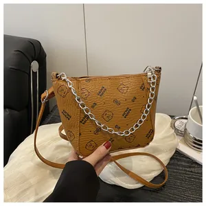 Détail d'un sac seau marron avec imprimé ours, cuir texturé et poignée en chaîne argentée