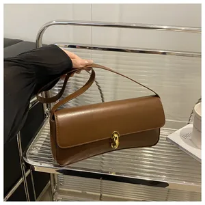 Detail of vintage brown leather baguette bag with a gold metal clasp shown on a model