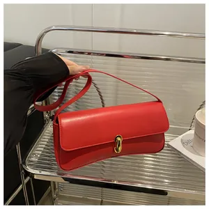 Detailed view of the red leather baguette bag featuring a gold oval lock and slim shoulder strap
