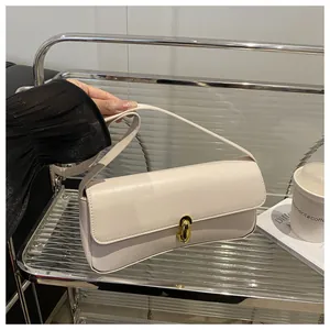 Detail of a cream faux leather baguette bag with a gold rectangular twist-lock clasp