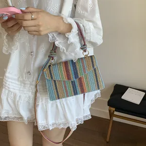 Detailed view of a multi-colored woven straw crossbody bag with light blue leather trim edge
