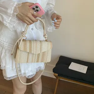Detail of a woven beige and brown crossbody bag with a knot handle and gold hardware