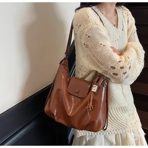 Détail d'un sac Hobo en cuir brillant marron foncé avec une étiquette carrée ANBAG