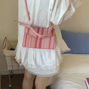 Detail shot of a pink striped woven crossbody bag with metallic gold hooks and strap