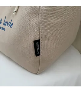 Close-up of beige canvas tote bag with blue C'est La Vie print and quality stitching