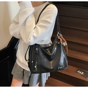 Détail du sac bandoulière en cuir noir avec pompons et plaque métallique de marque