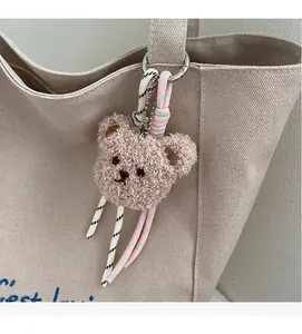 Detail of cute plush bear charm with woven ropes on beige canvas tote bag handle