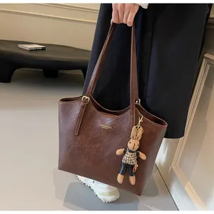 Détail d'un cabas marron foncé avec texture cuir, logo doré et breloque lapin mignonne