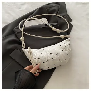 Detail of white dumpling crossbody bag with black bow patterns and rope shoulder strap