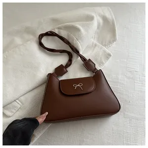 Dettaglio della fibbia a fiocco argento e tracolla intrecciata su borsa in pelle marrone