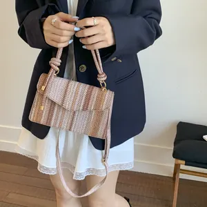 Detail of woven gradient handbag showing knot handle and textured straw material