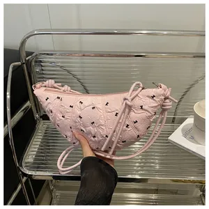 Detailed shot of pink pleated crescent bag featuring black bow patterns and rope strap