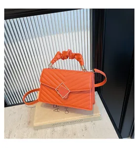 Close-up of orange quilted crossbody bag with pleated handle and double diamond metal lock