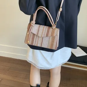 Detail of striped straw woven crossbody bag with metallic studs and top handle strap