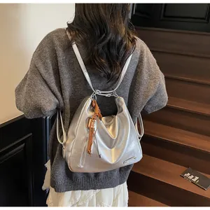 Détail du sac à dos argenté brillant avec pompon marron et fermeture éclair latérale