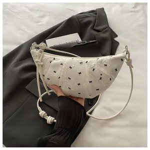 Close-up of white pleated crescent bag with black bow embroidery and knot strap