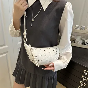 White crescent crossbody bag with black bow patterns and knotted rope shoulder strap
