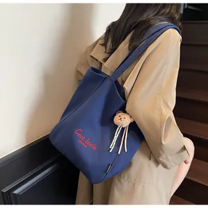 Detail of dark blue canvas tote bag with red lettering and small bear plush pendant
