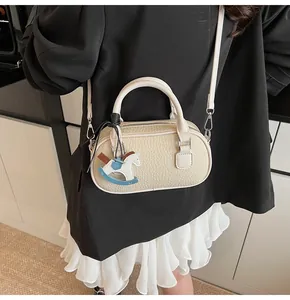 Detail of cream white mini Boston bag with pebbled leather texture and rocking horse charm
