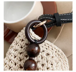 Detail van gevlochten tas met lederen riem, witte stiksels en houten kralen voor decoratie