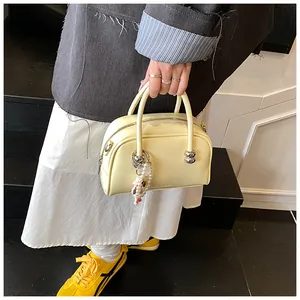Close-up of a pale yellow square handbag with beaded charm and silver zipper detail