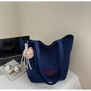 Detail of dark blue canvas tote bag with red embroidery and plush bear charm accessory