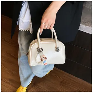 Detail of glossy beige square handbag with pearl doll charm and metal hardware