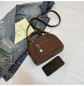 Détail du sac bowling marron foncé avec pendentif cœur et texture cuir mat