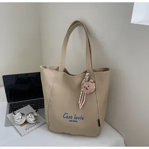 Detail of khaki canvas tote bag featuring C'est lavie print and plush bear charm
