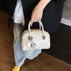 Chic creamy white patent leather handbag with pearl charm shown in a professional setting