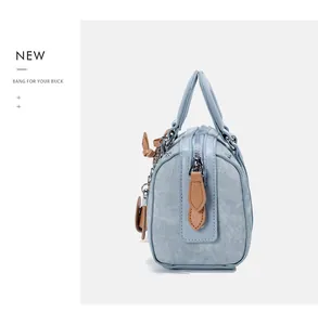 Detail of light blue textured Boston bag with brown leather handles and metal zipper
