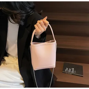 Detail van lichtroze bucket bag met litchi-textuur en kettingriem bij een model