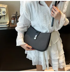 Detail view of black textured leather shoulder bag with silver buckle on white dress