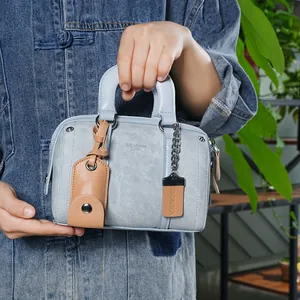Close-up of light blue denim Boston bag featuring leather handles and brand hangtags