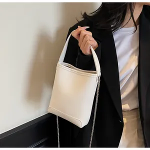 Detail van witte bucketbag met generfde ledertextuur en zilveren ketting schouderriem
