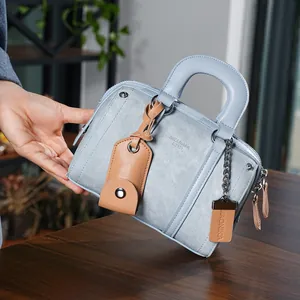 Detail view of light blue denim texture Boston bag with leather handles on wood surface