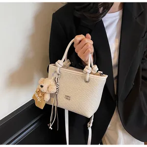 Detailed close-up of a cream woven bucket bag featuring a knot-handle and plush bear charm