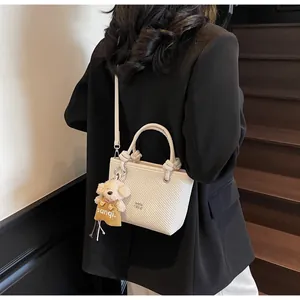 Detail of cream woven bucket bag with cute dog pendant worn with a black blazer
