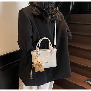 Detail of white textured bucket bag with brown teddy bear charm on black blazer