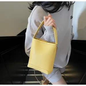 Detail van gele crossbodytas van generfd leer met zilveren ketting en vast handvat